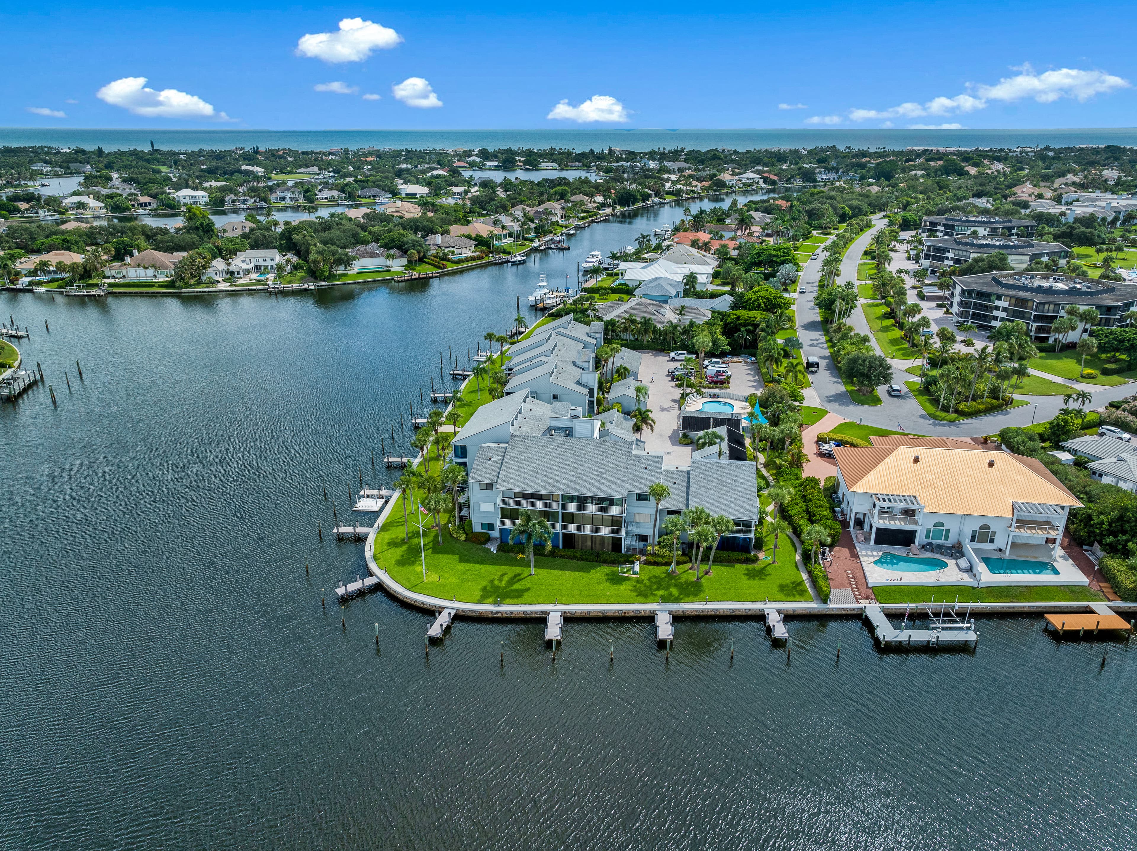 Aerial view of a waterfront condo complex with private docks on a wide waterway, with canal homes and the Atlantic Ocean beyond.