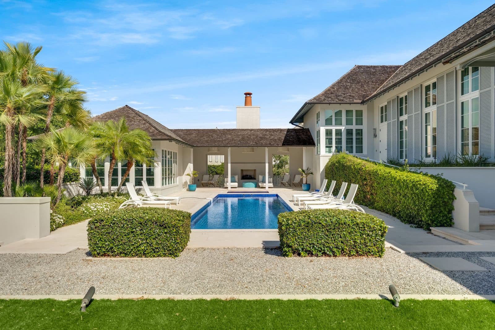 Exterior view of a white home with a blue swimming pool, covered patio, and tropical landscaping.