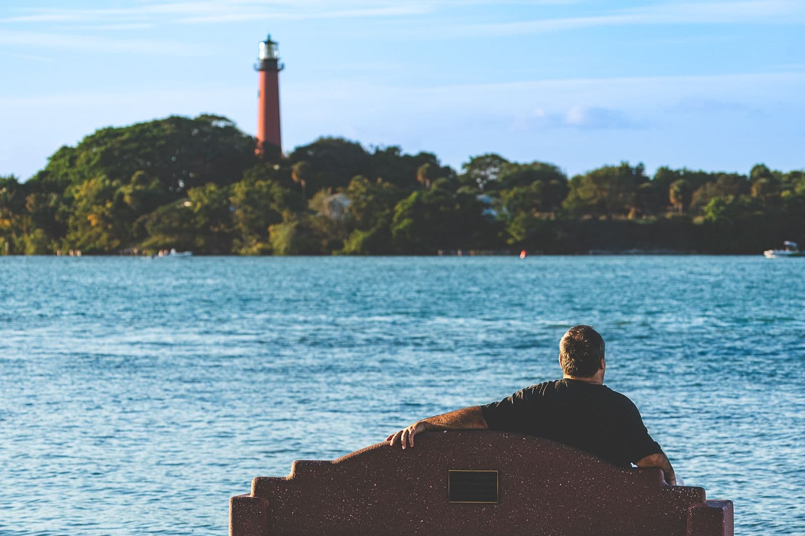 Man sitting by water looking at Jupiter Lighthouse.