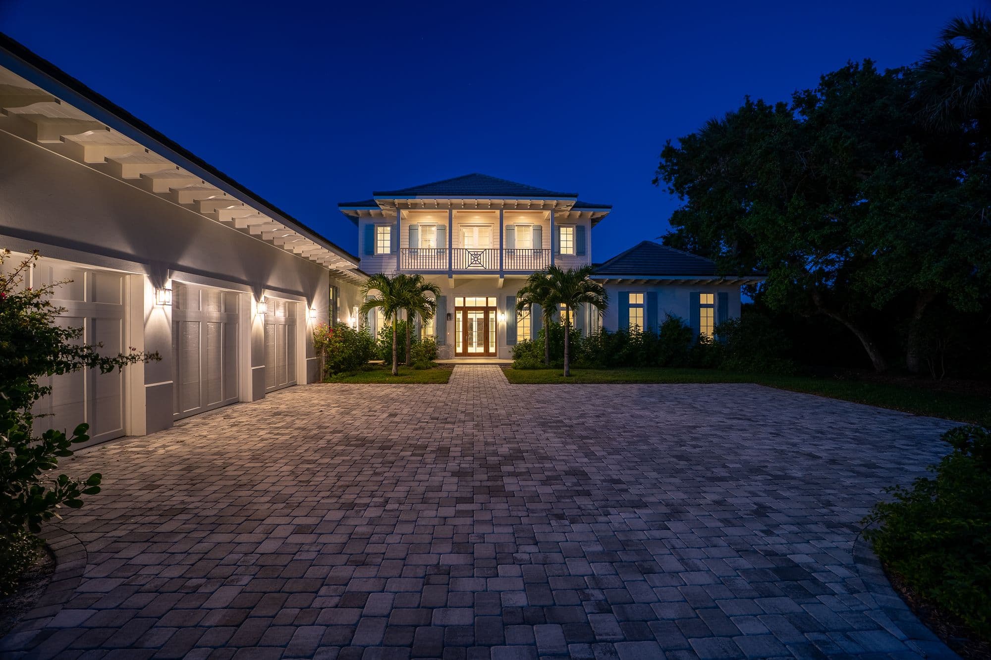 Two-story house exterior at twilight with a prominent balcony and paver driveway.