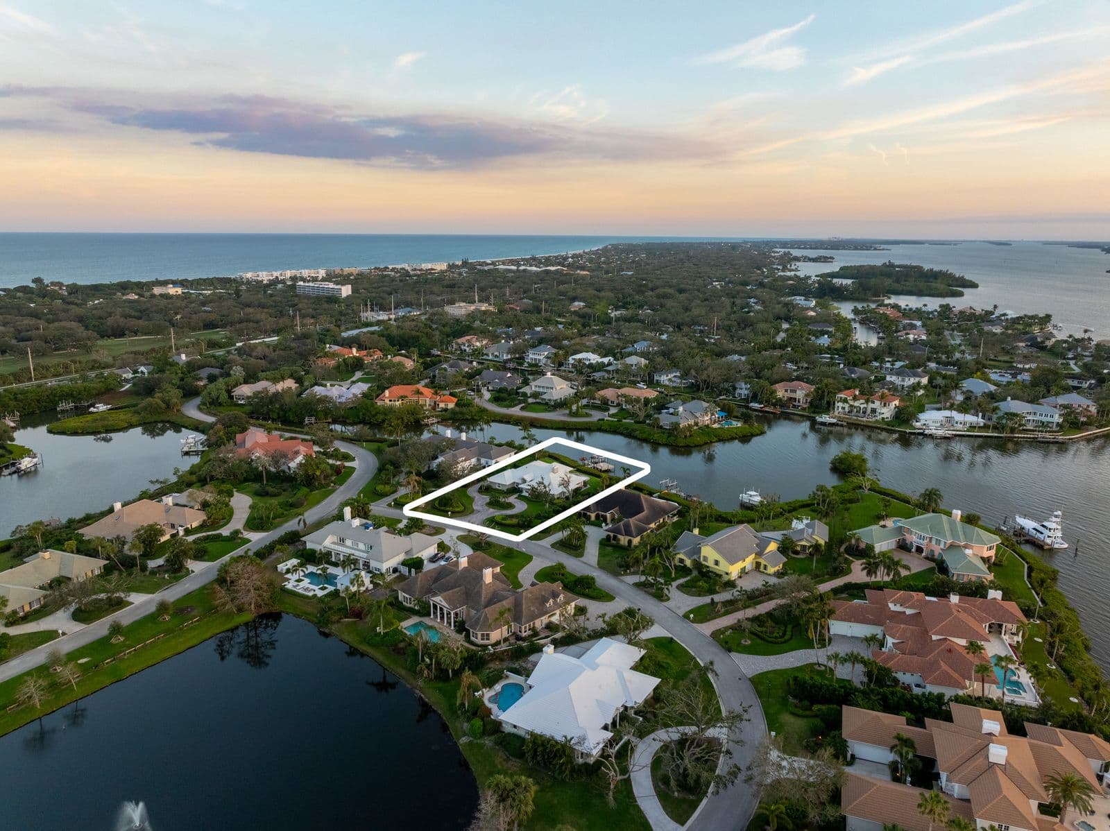 Aerial view of a large residential area with waterfront homes, meandering canals leading to the ocean, under a twilight sky.