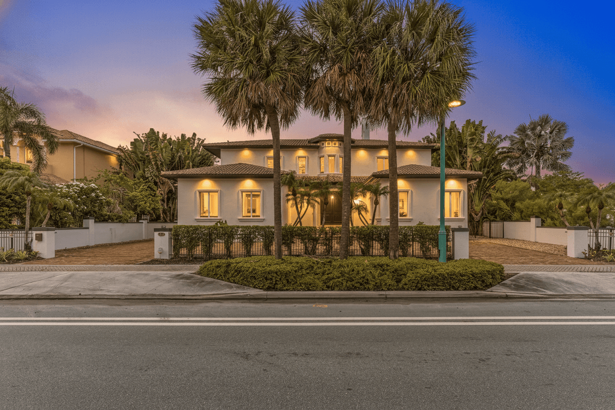 Two-story house exterior at dusk, with lit windows and three tall palm trees in front.